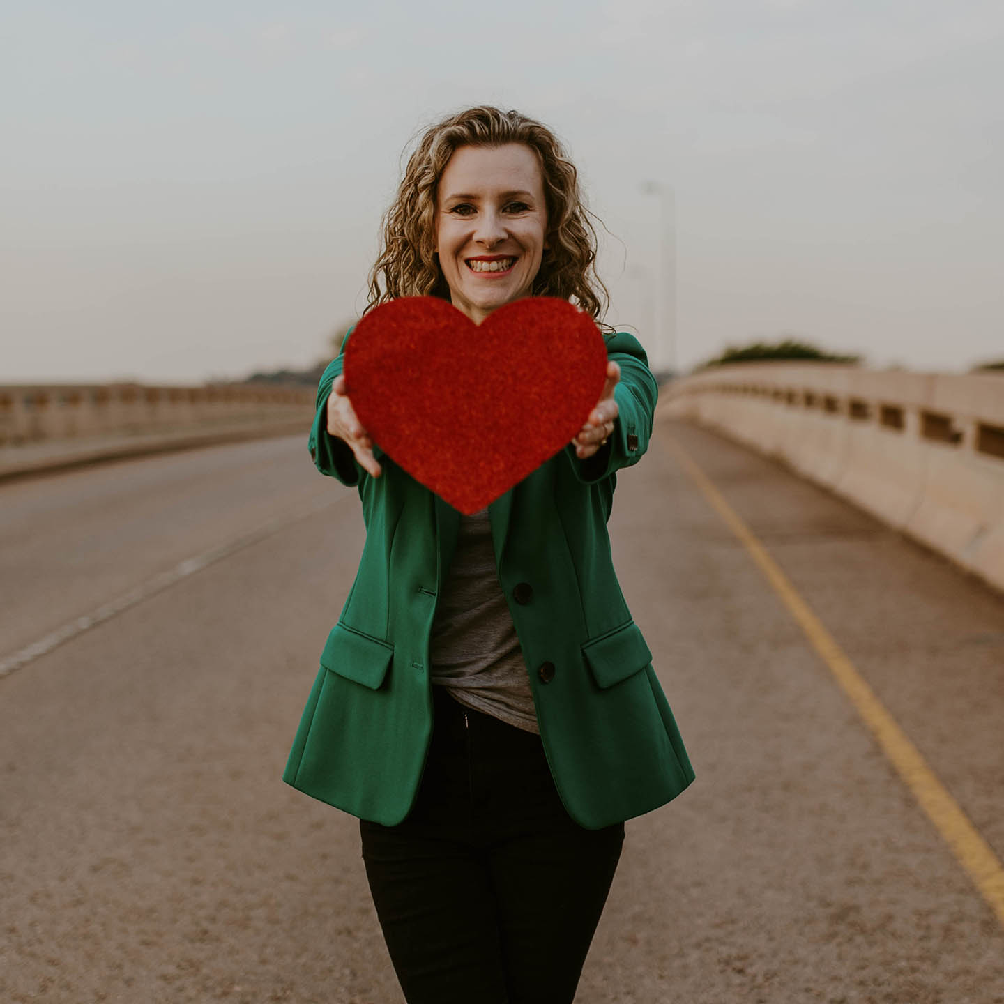 woman wearing a green jacket holding up a red heart